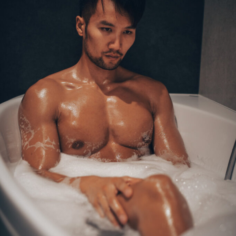 A muscular Asian man relaxes in a deep foam bath, his powerful physique softened by white bubbles and warm water. Manhood Glimpse by Photographer Slovakia.