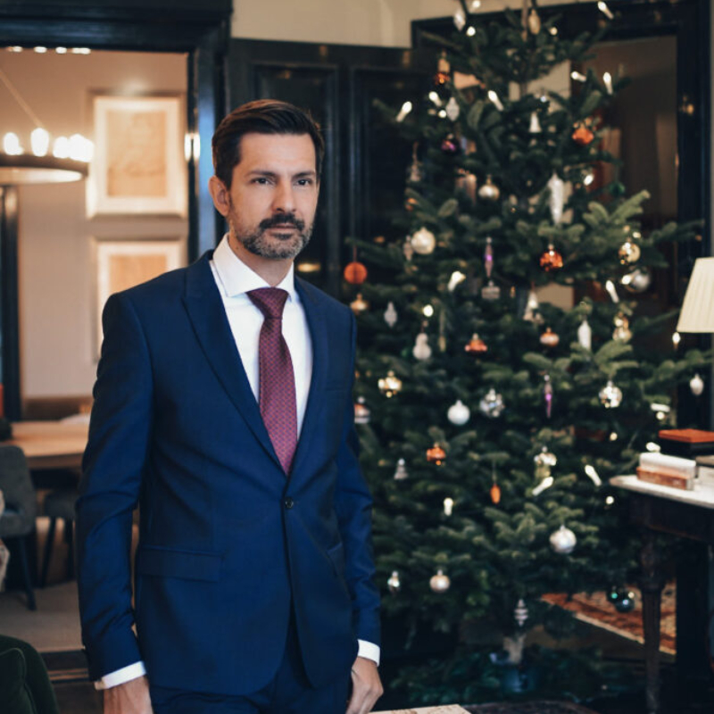 Handsome male model in an elegant blue suit standing next to a Christmas tree. High-quality male aesthetics and lifestyle photography.