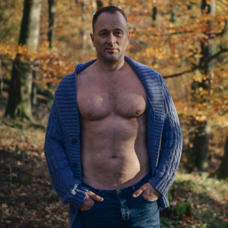 A middle-aged man in a sweater stands among many colorful trees during a vibrant autumn day. Elite Member Preview.