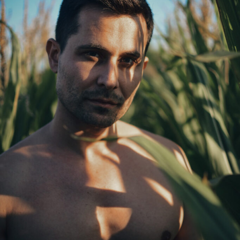 Handsome male model posing shirtless outdoors with beautiful sunlight and shadows on his chest. Exclusive outdoor male photography.
