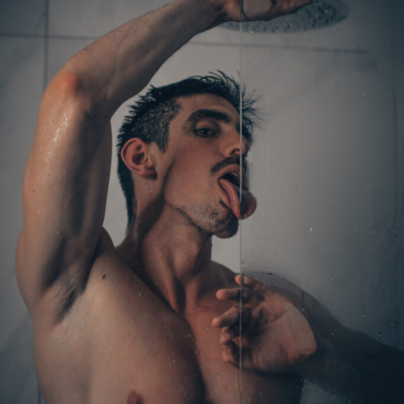 Sensual and intimate portrait of an athletic male model behind wet shower glass. Premium male photography preview.